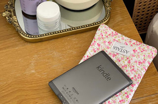Astala Luna Blossom Kindle Pouch with pink floral print holding a Kindle on a wooden bedside table