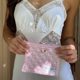 Pink gingham quilted makeup pouch held by a woman wearing a lace white slip dress from Astala Luna.