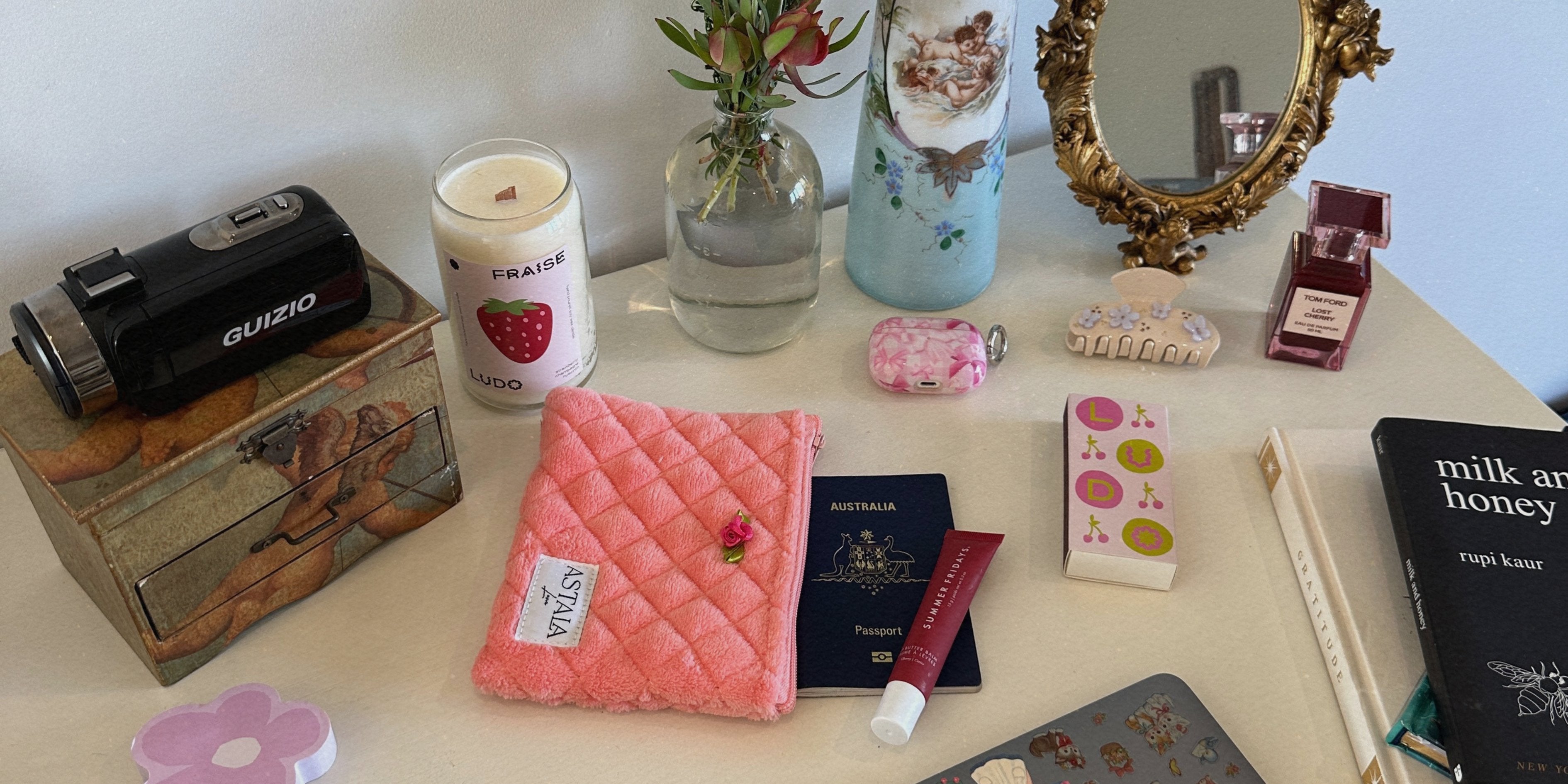 Image of a desk laid out with lots of items including our astala luna pouch, a passport, lipbalm, camera, book, hair clip and airpods.